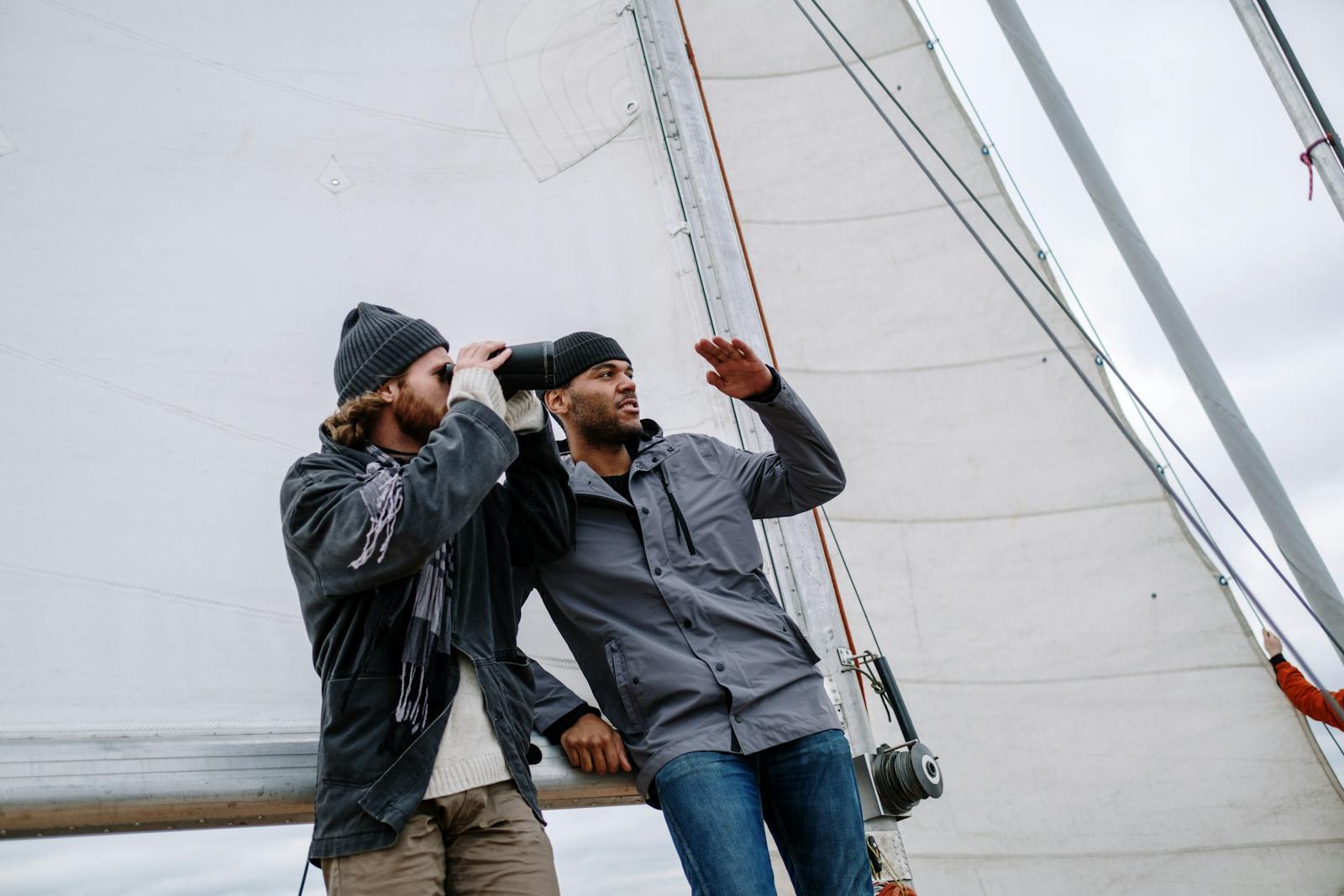 Two men on a sailboat, engaging in a nautical adventure under clear skies.