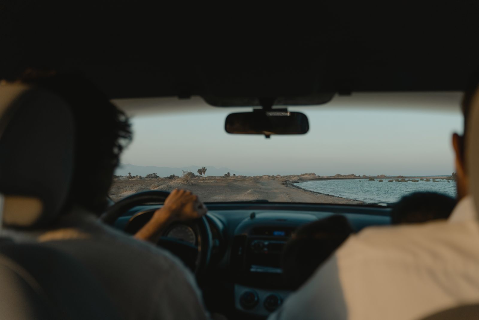 Interior car view of a scenic drive along a coastal road at sunset.