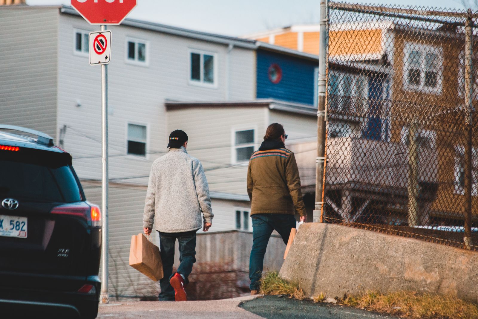 Back view of anonymous people promenading on street of town with modern car and residential houses