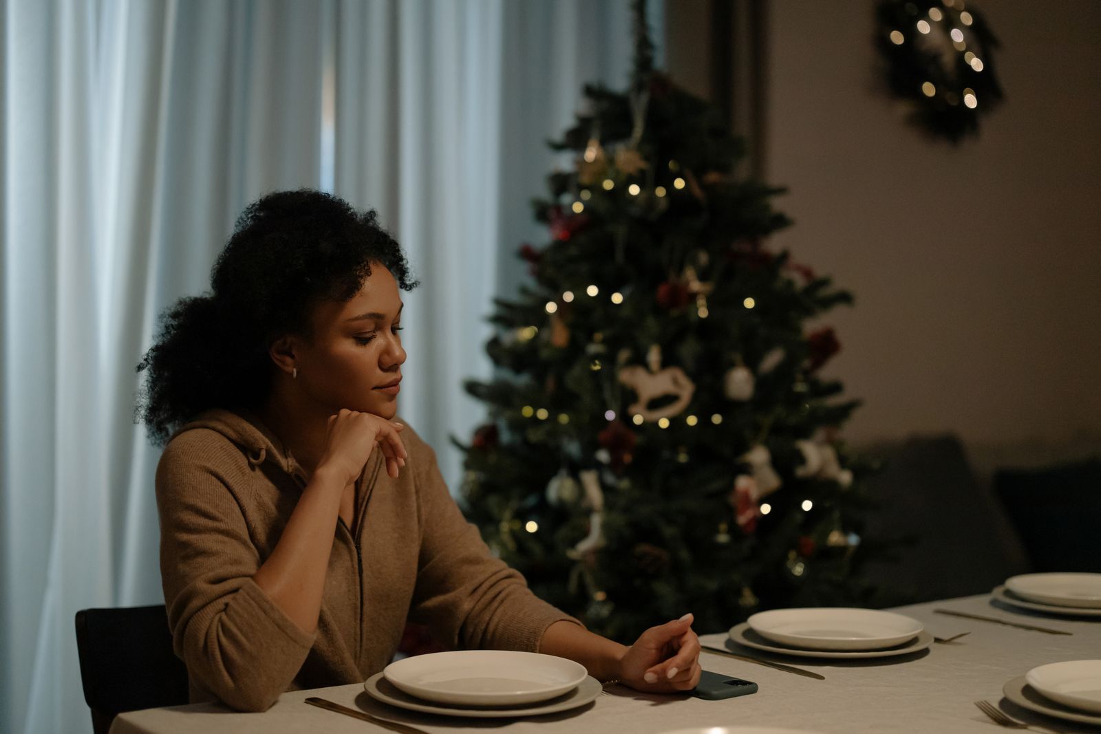 African American woman sitting by a Christmas tree with a set dining table.