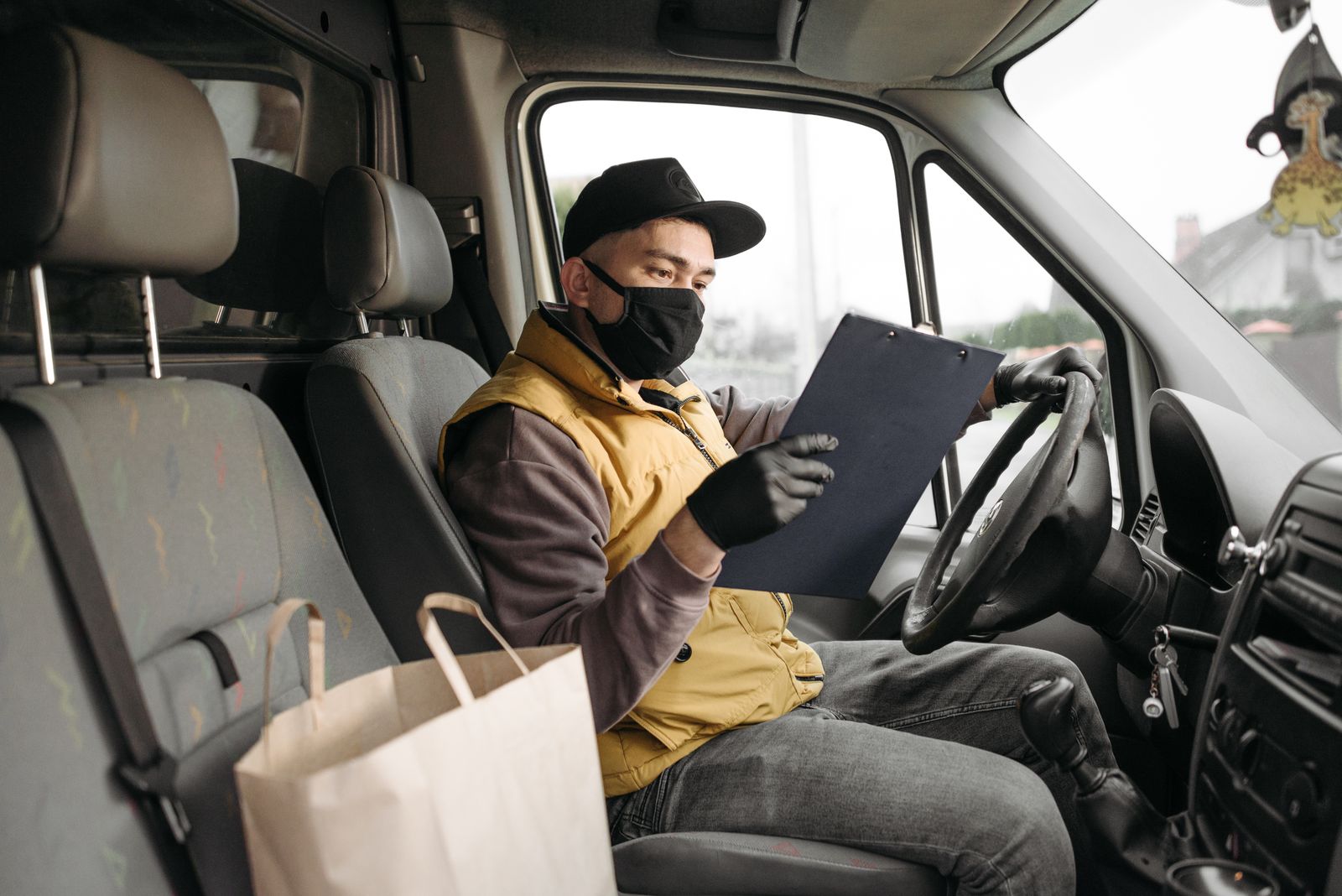 Masked delivery driver reading clipboard in a van during the day.