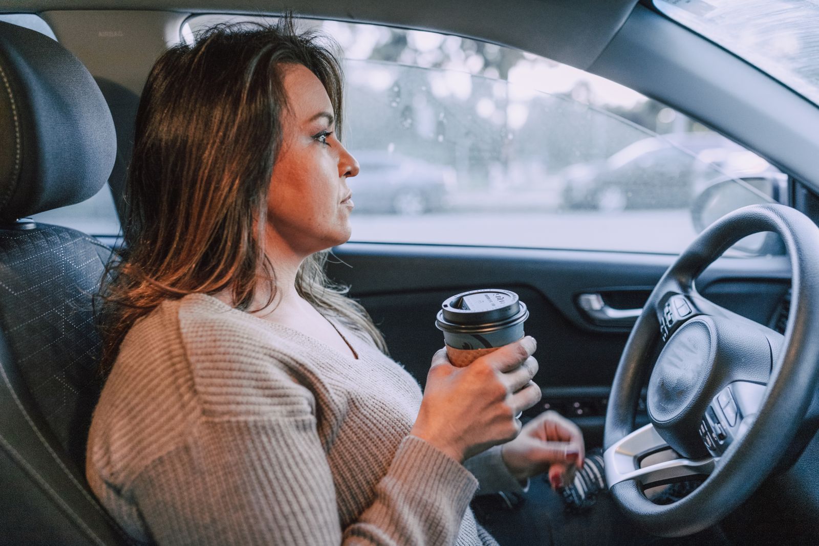 A woman in a car holding a disposable coffee cup, showing focus.