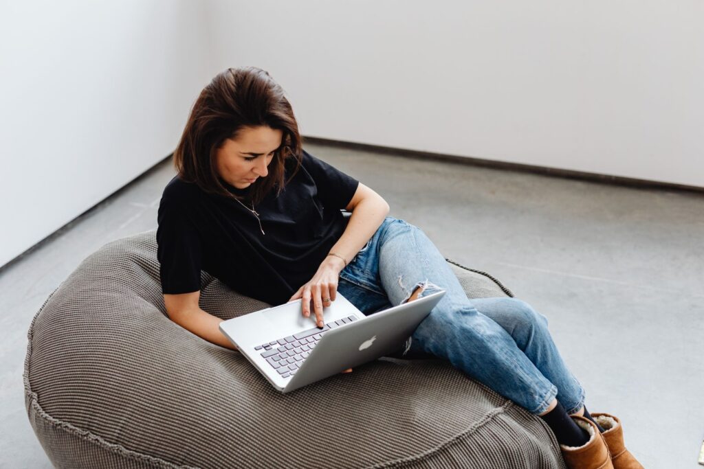 Casual working from home setup with a young woman using a laptop on a bean bag.