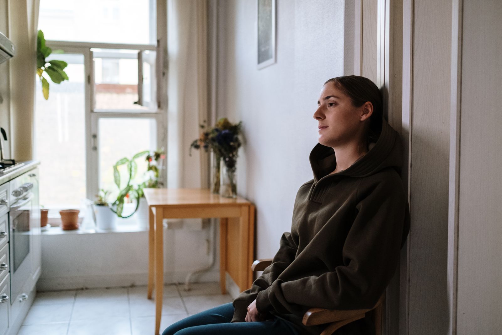 Pensive woman in a hoodie sitting indoors by a window, capturing a moment of reflection.