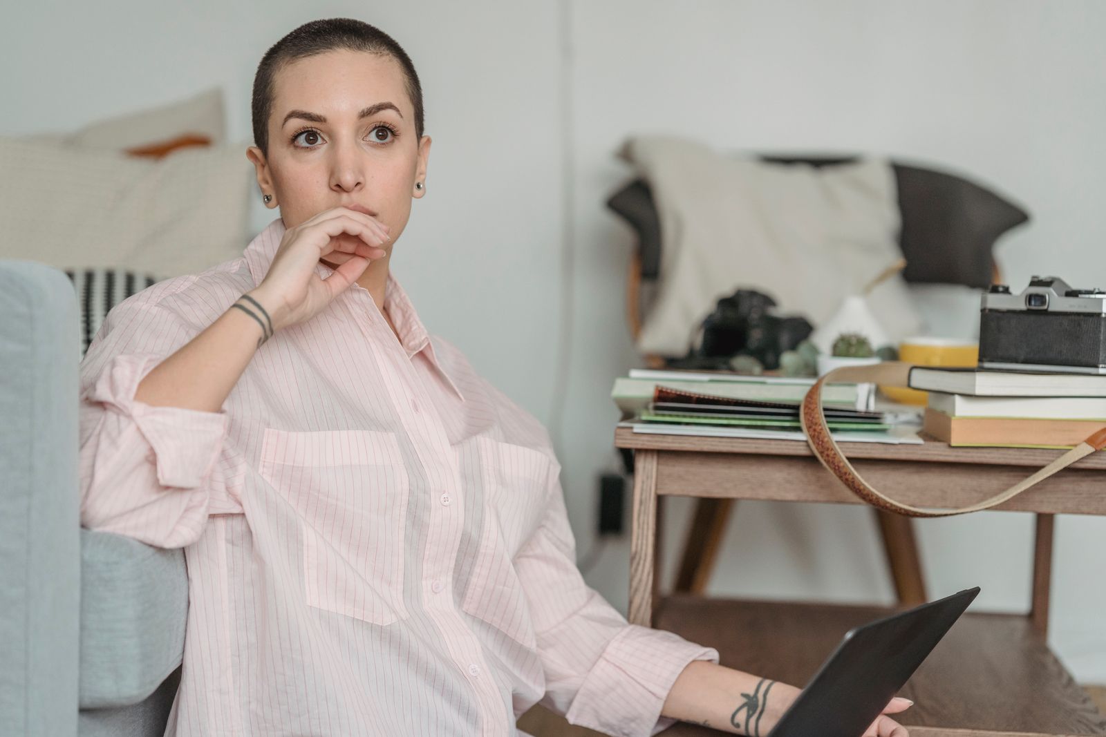 Serious young female freelancer with short dark hair in shirt touching lips and looking away thoughtfully while working online on laptop at home