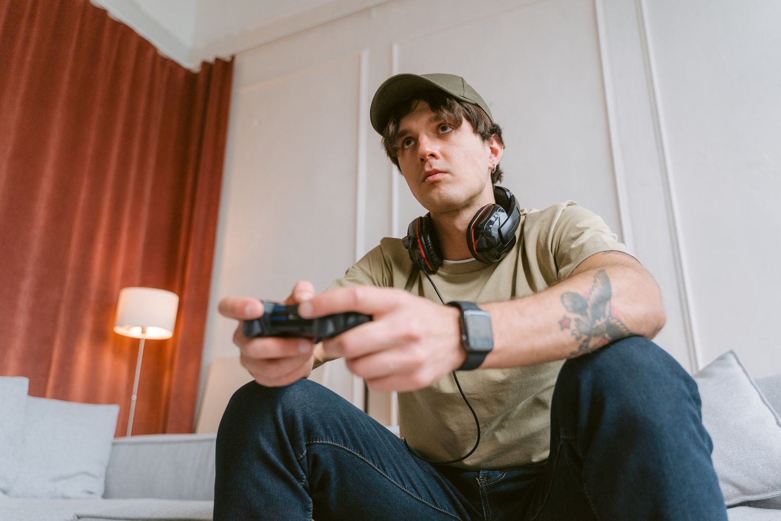 Casual young man with a game controller and headphones focused on playing a video game indoors.