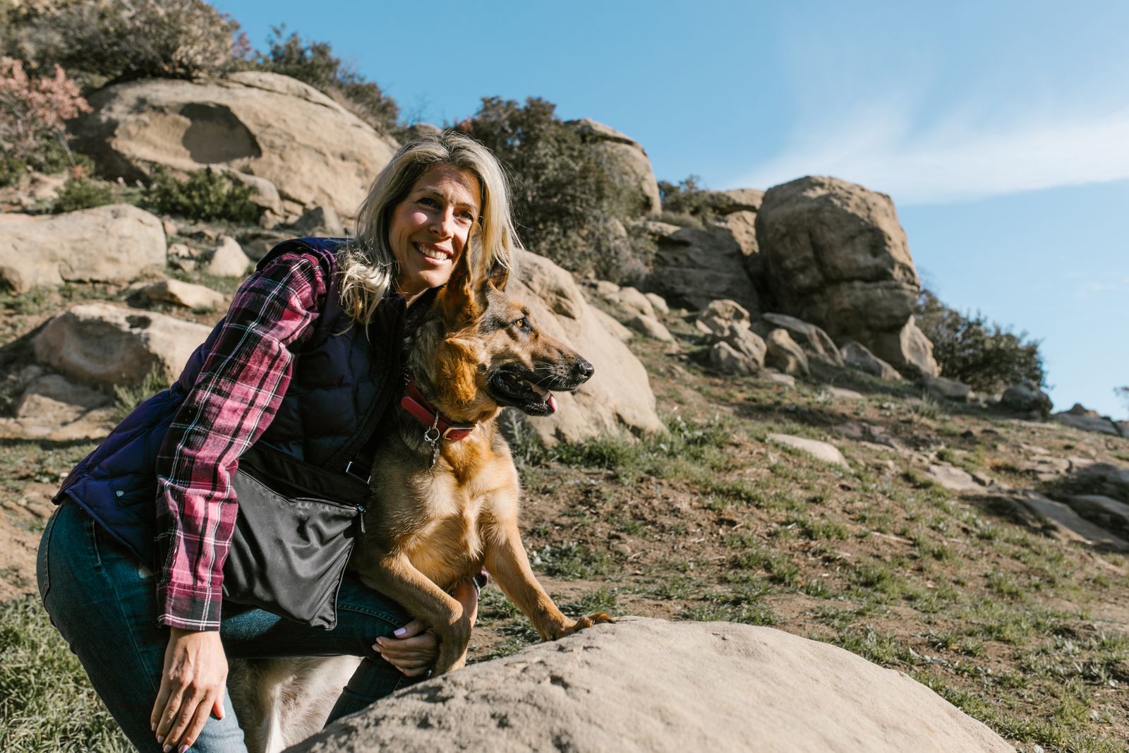 Smiling woman with her German Shepherd at rocky outdoor location on a sunny day.