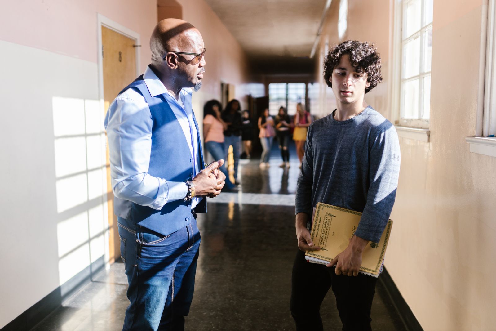 A teacher and student engaged in conversation in a bright school hallway.