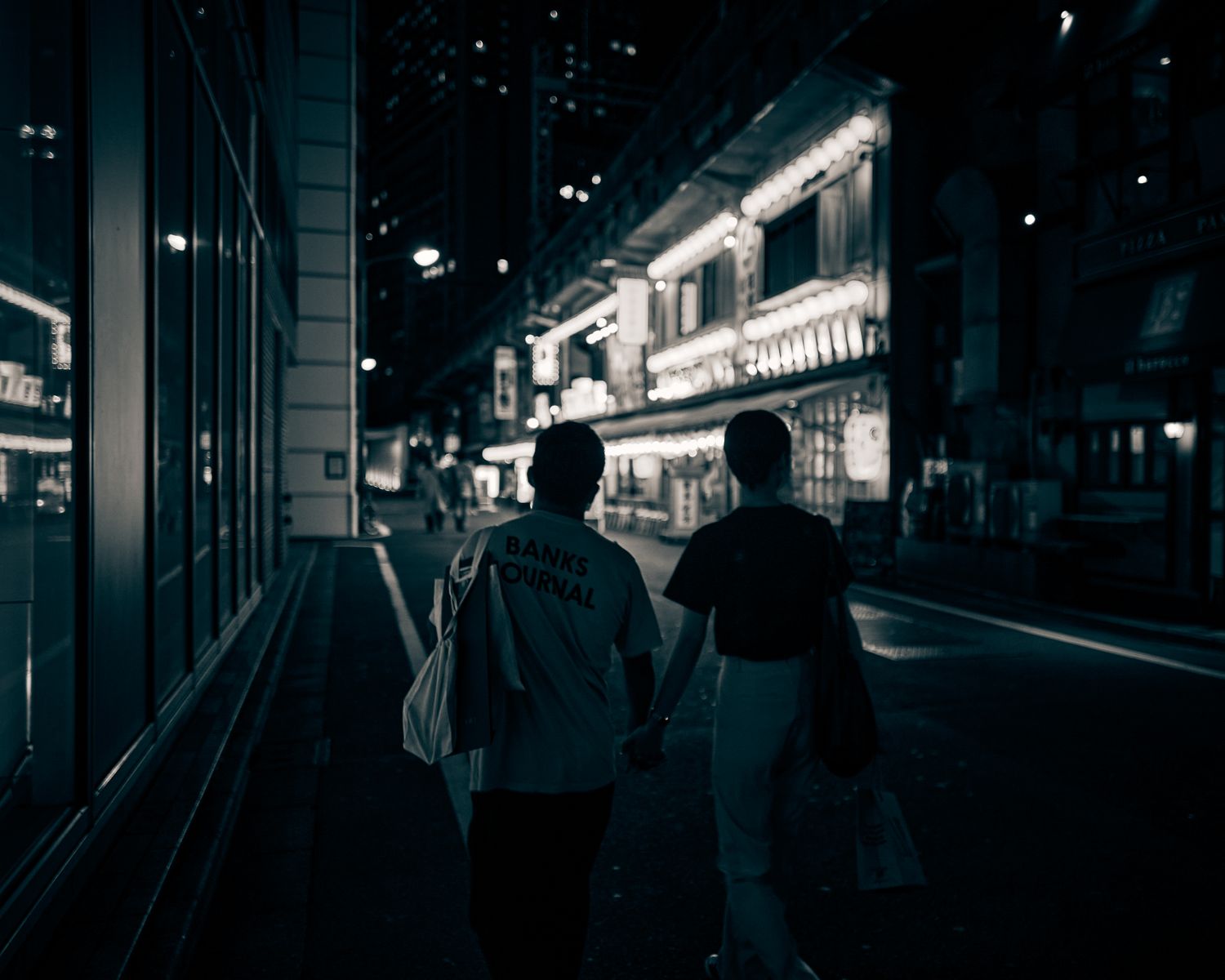 A couple walking along a bright, neon-lit street at night, holding hands and enjoying the city ambiance.