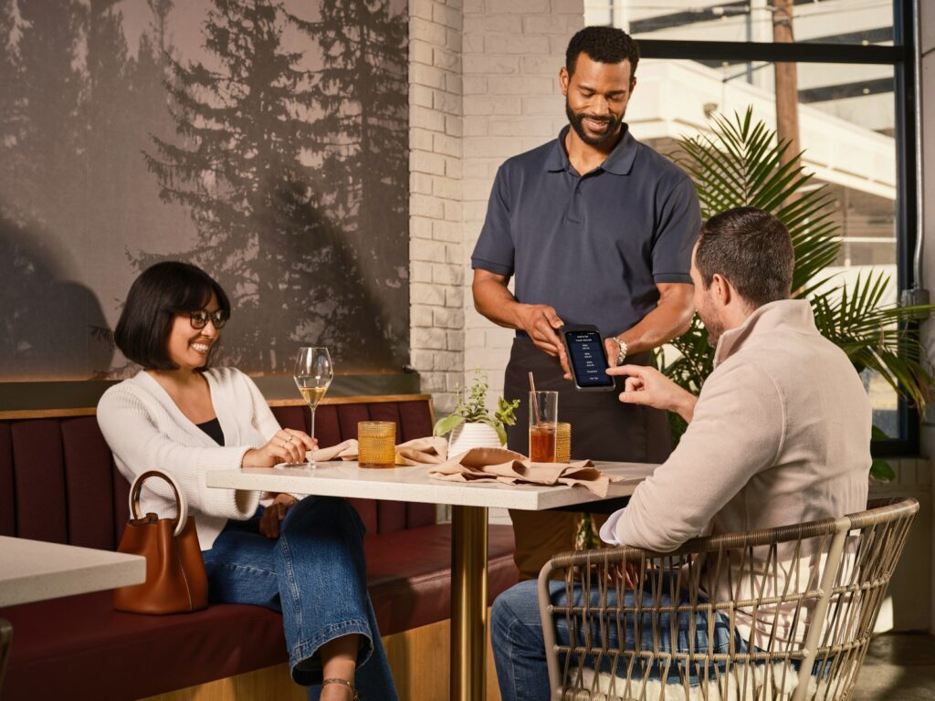 Waiter shows tablet to couple at restaurant table.