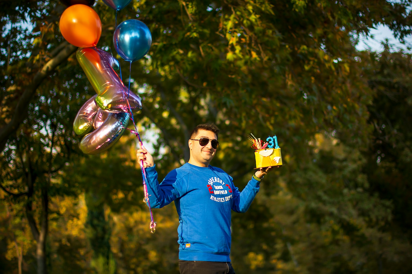 a man in a blue shirt holding a box and balloons