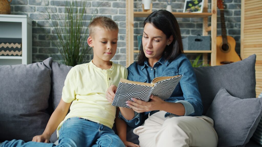 Mother and son reading a book together on the couch.