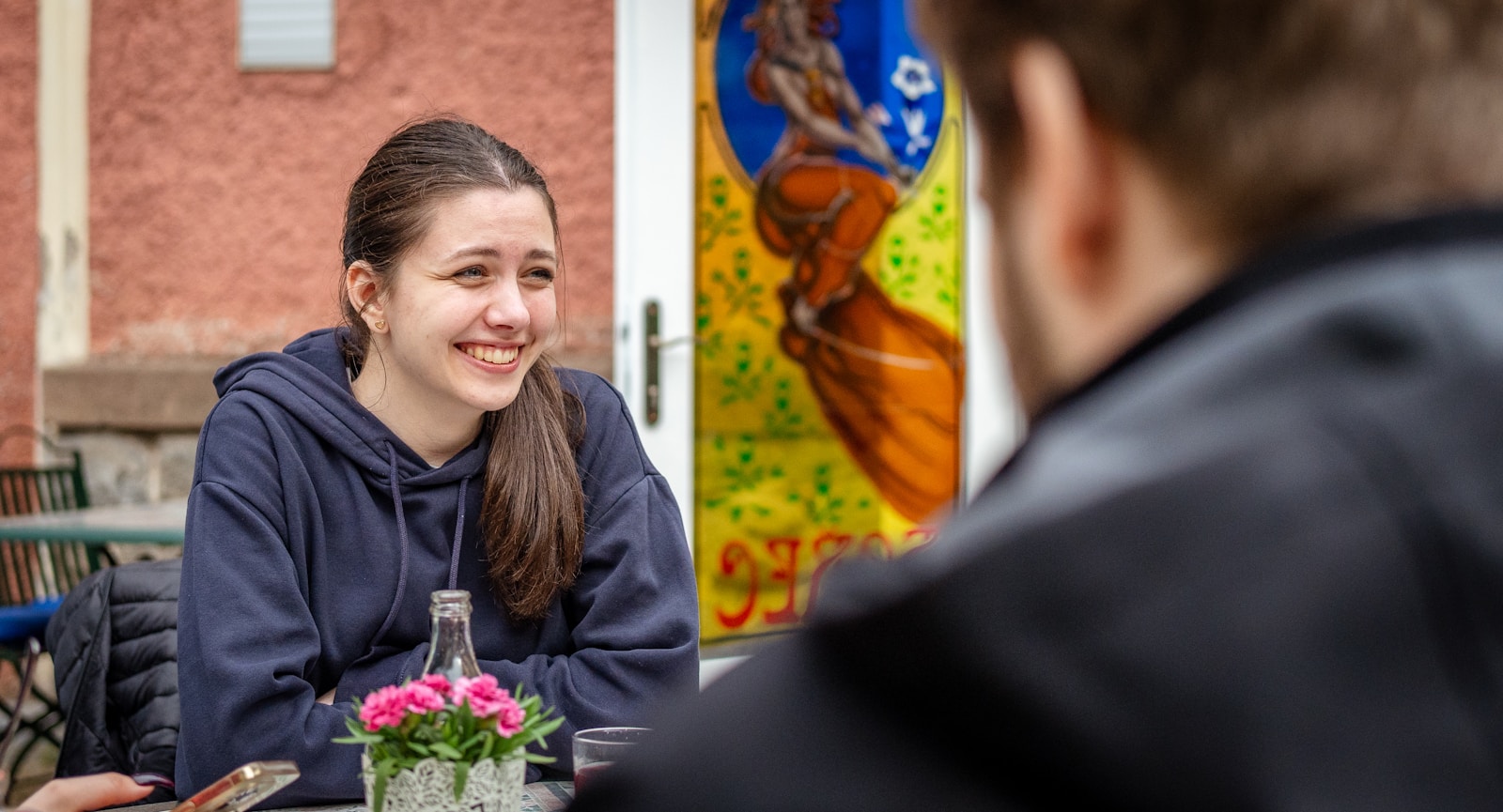 Young woman smiling while sitting at an outdoor cafe.