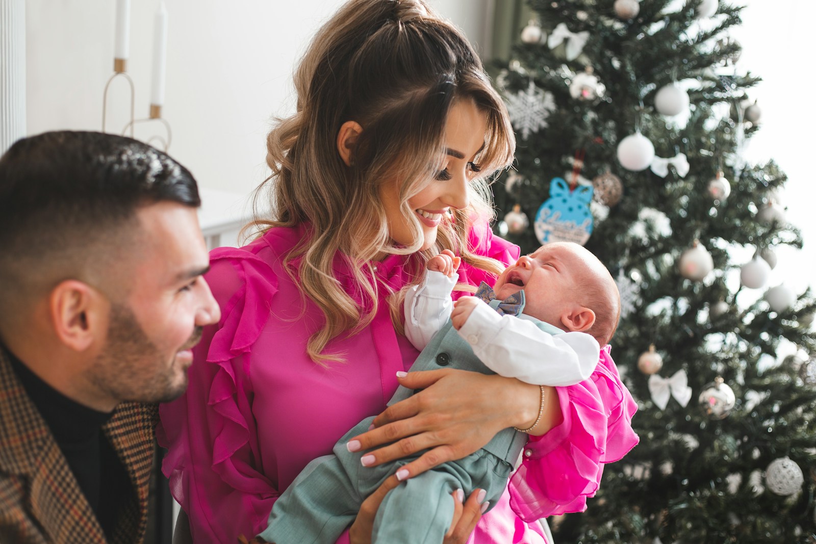 Parents holding their newborn baby near christmas tree