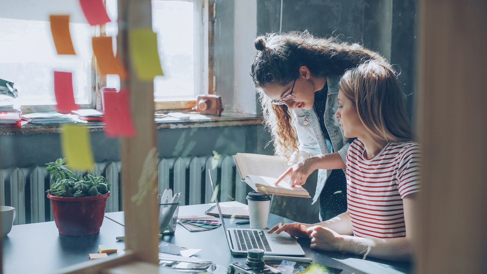 Two women collaborate over a laptop in an office.