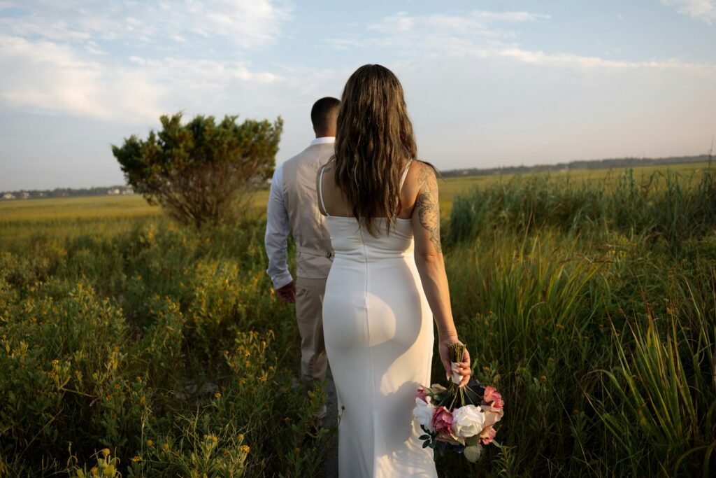A bride and groom walking through a field