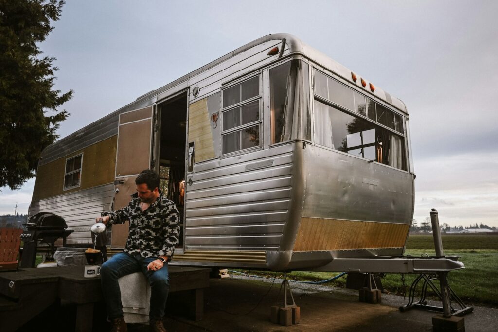 Man sits outside vintage silver camper trailer.