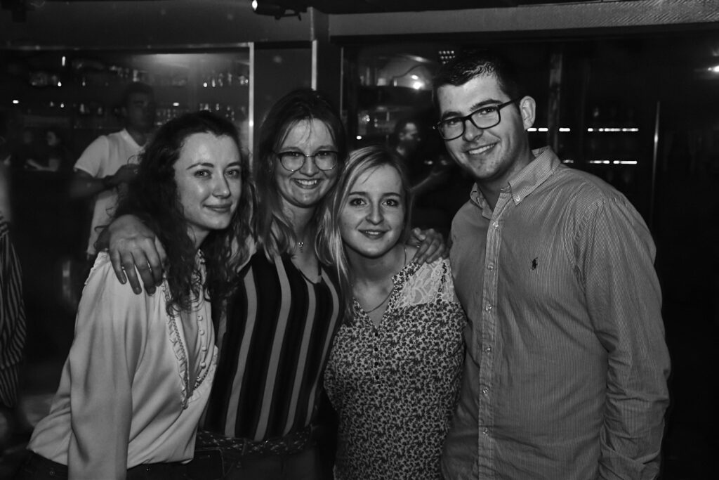 Four friends smiling together in a dimly lit room.