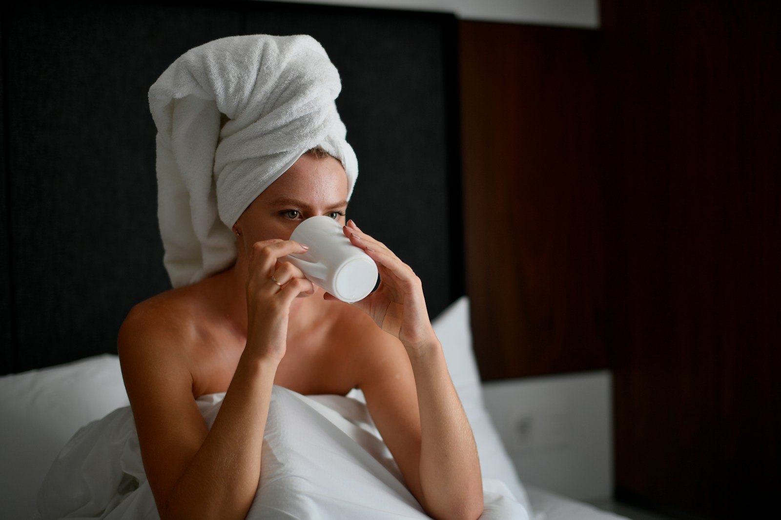 Woman with towel on head drinks coffee in bed