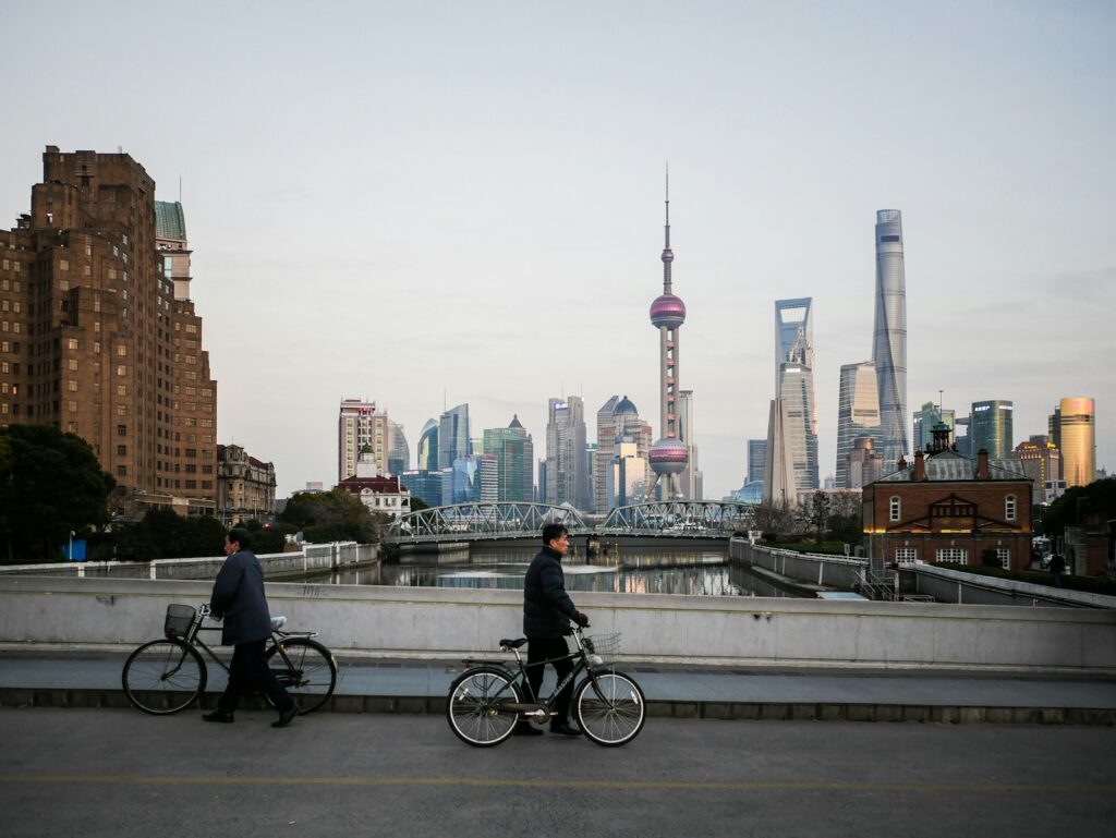 People with bicycles on a bridge with a shanghai skyline.