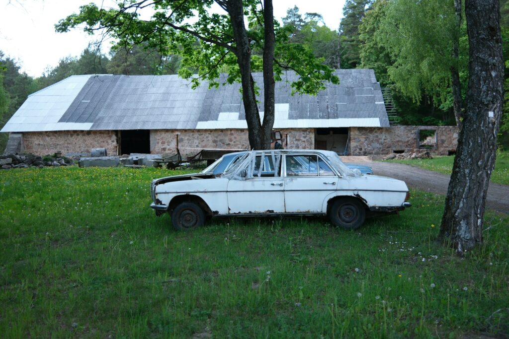 Old rusty white car parked in front of rustic building.