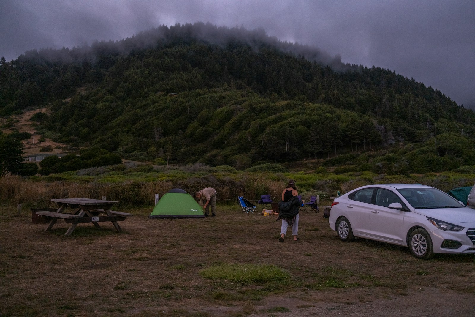 a woman and a man standing next to a tent and a car