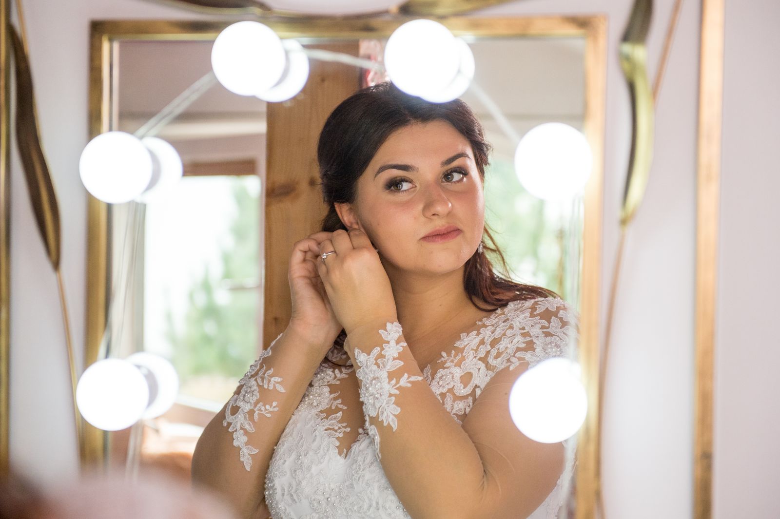 Bride adjusting earrings while looking at her reflection in a mirror before wedding.