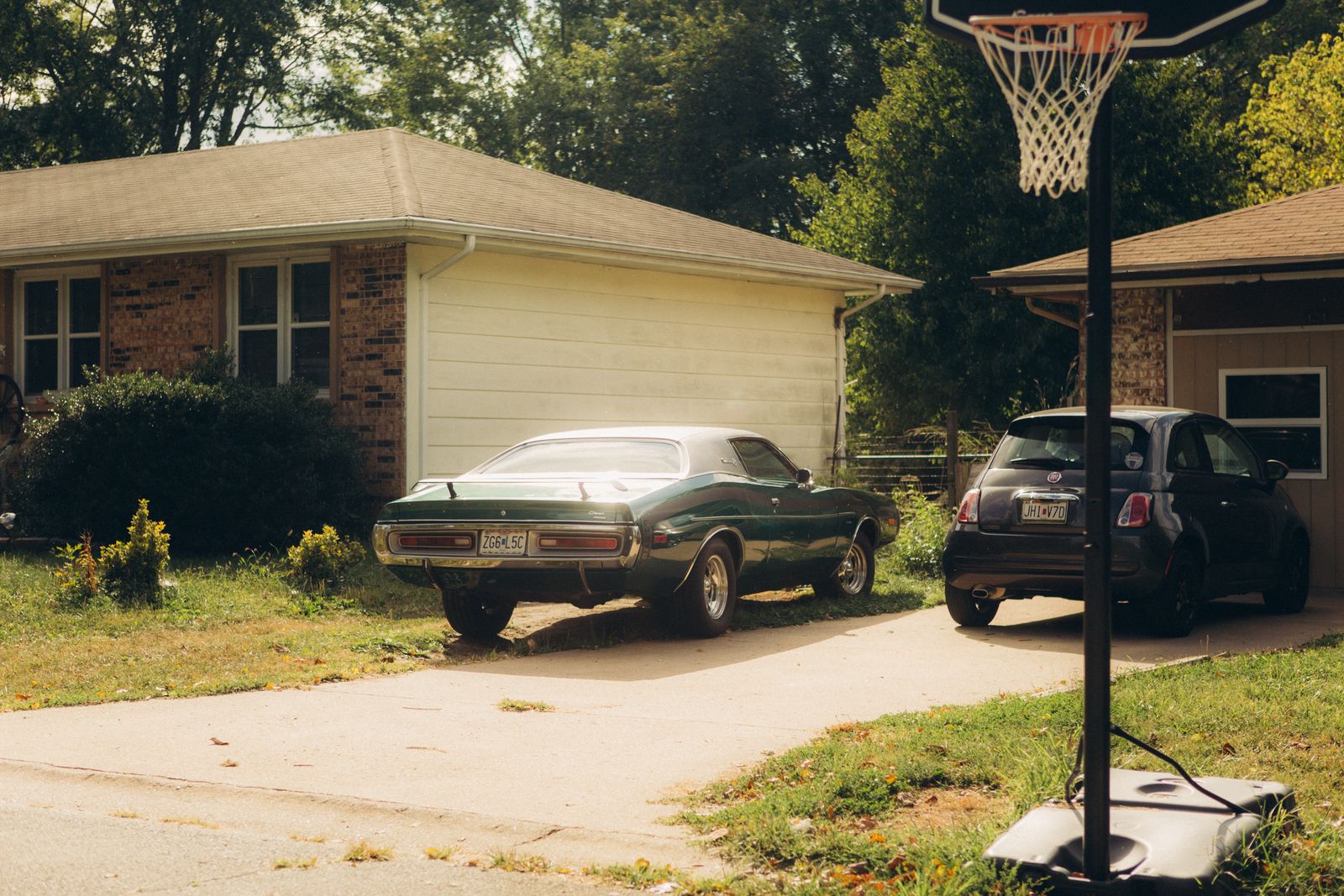 A serene suburban driveway featuring a classic car and a basketball hoop under a clear sky.