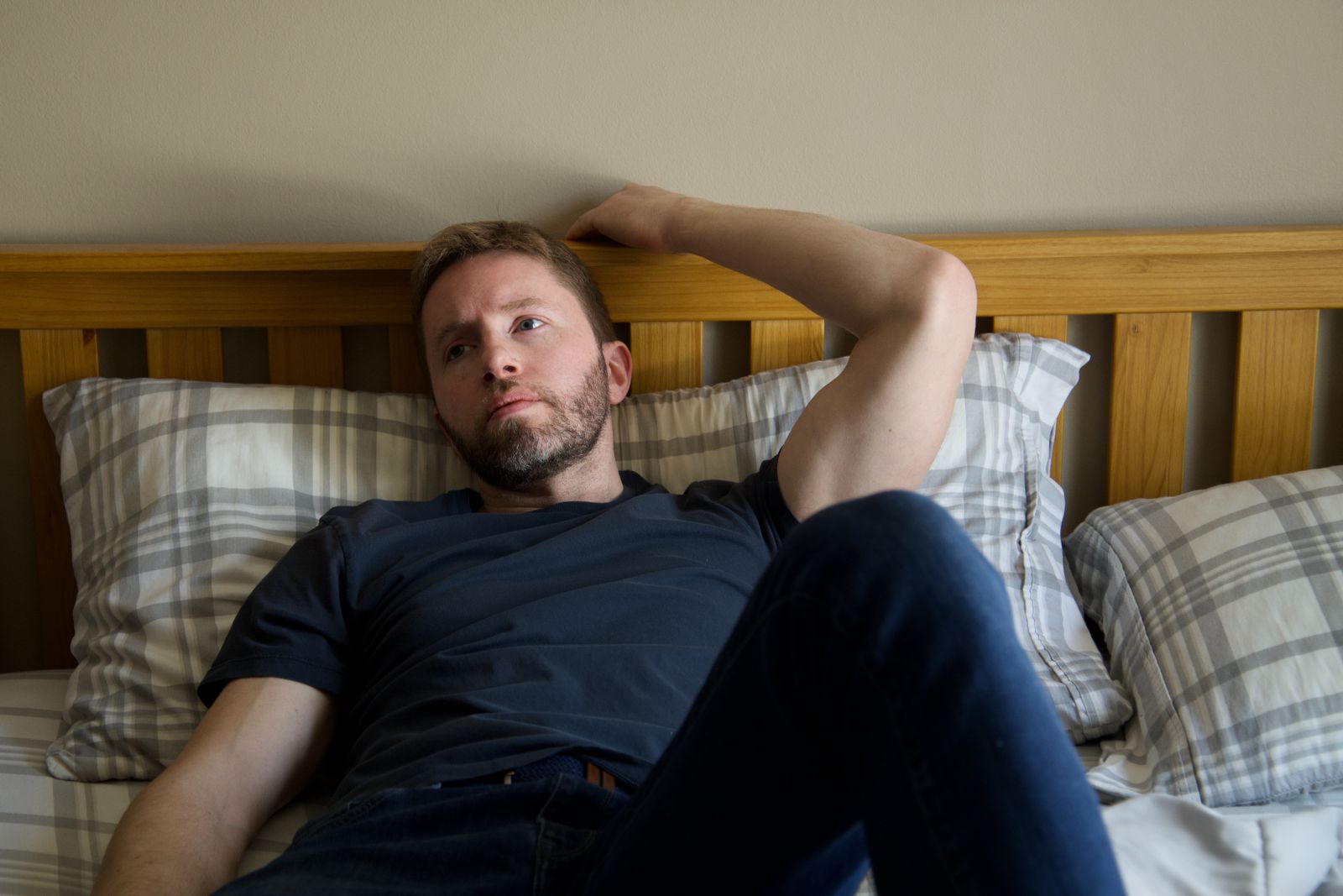 A man with a beard and mustache lying on a bed, resting and wearing casual clothing.