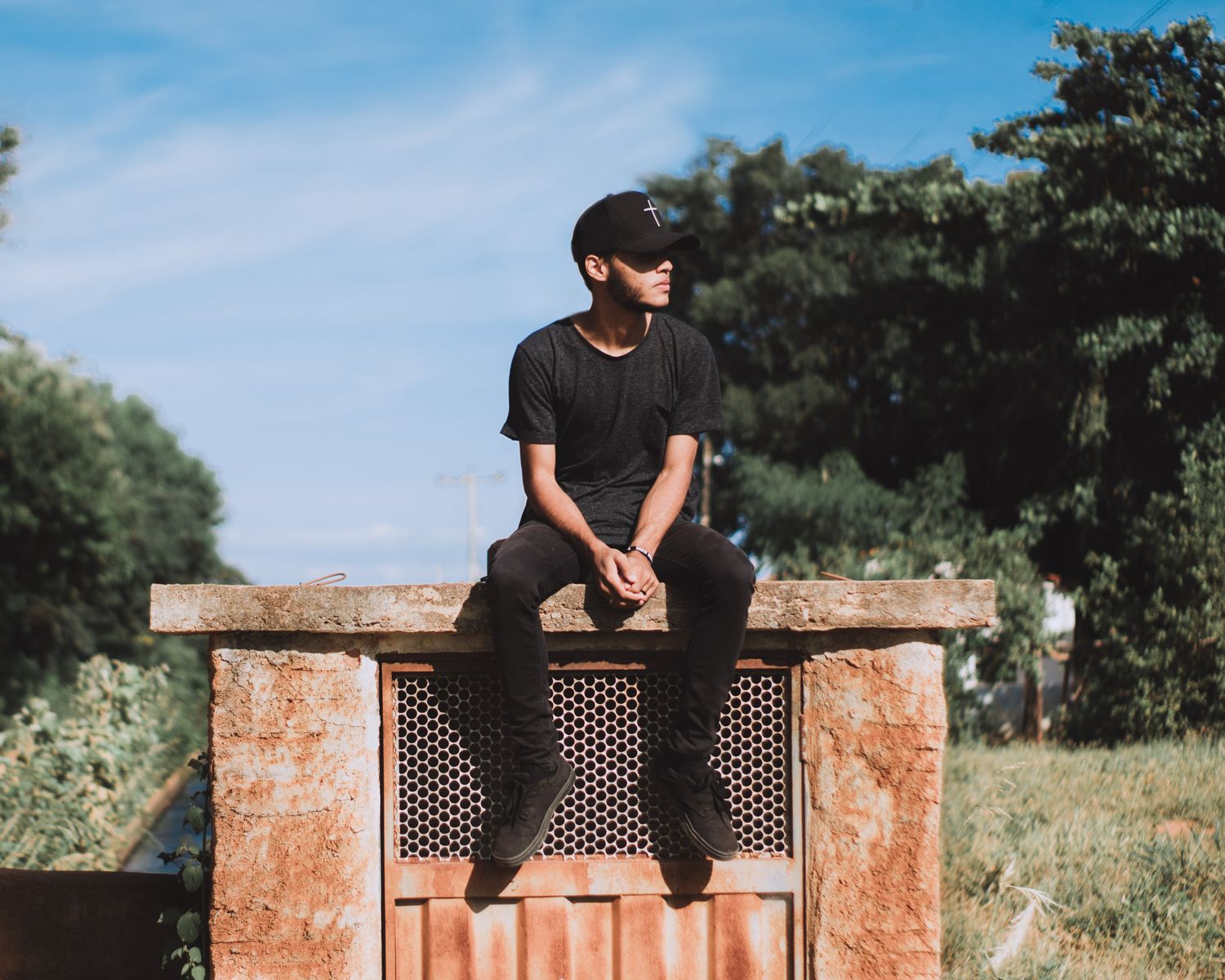 Man in black casual wear sitting on a rustic outdoor structure under the blue sky.