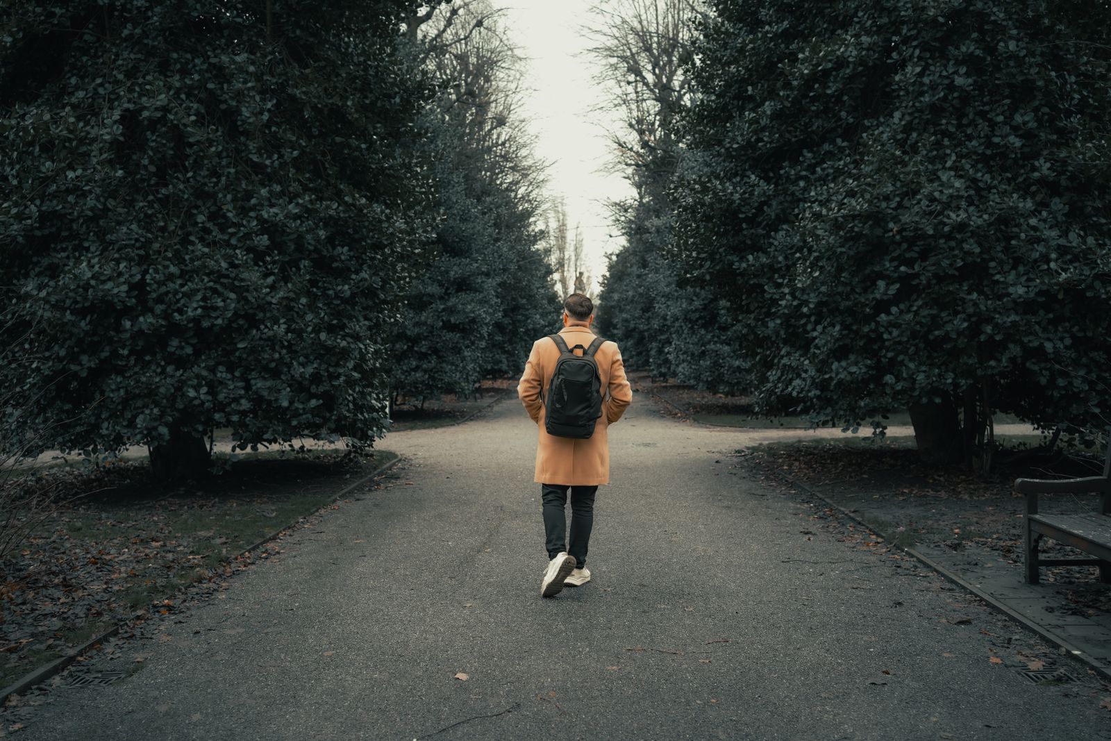 A man in a coat and backpack walks a path in Chester's autumn park.