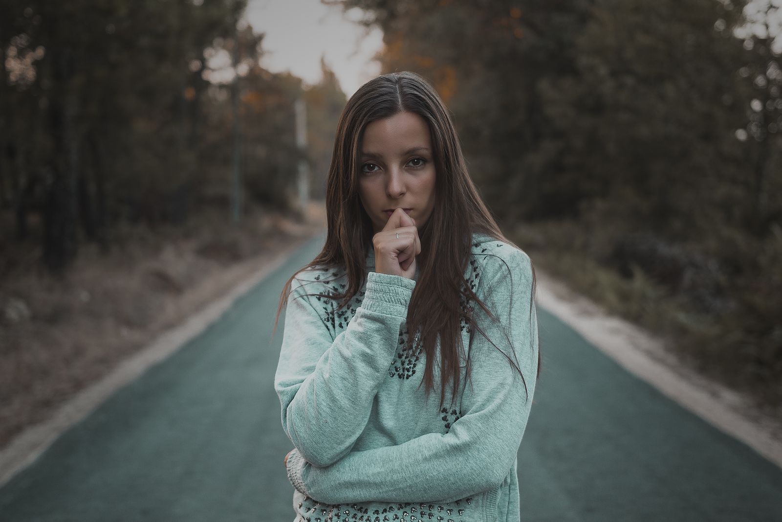 Pensive woman standing on a quiet forest road, lost in thought. Outdoor portrait.