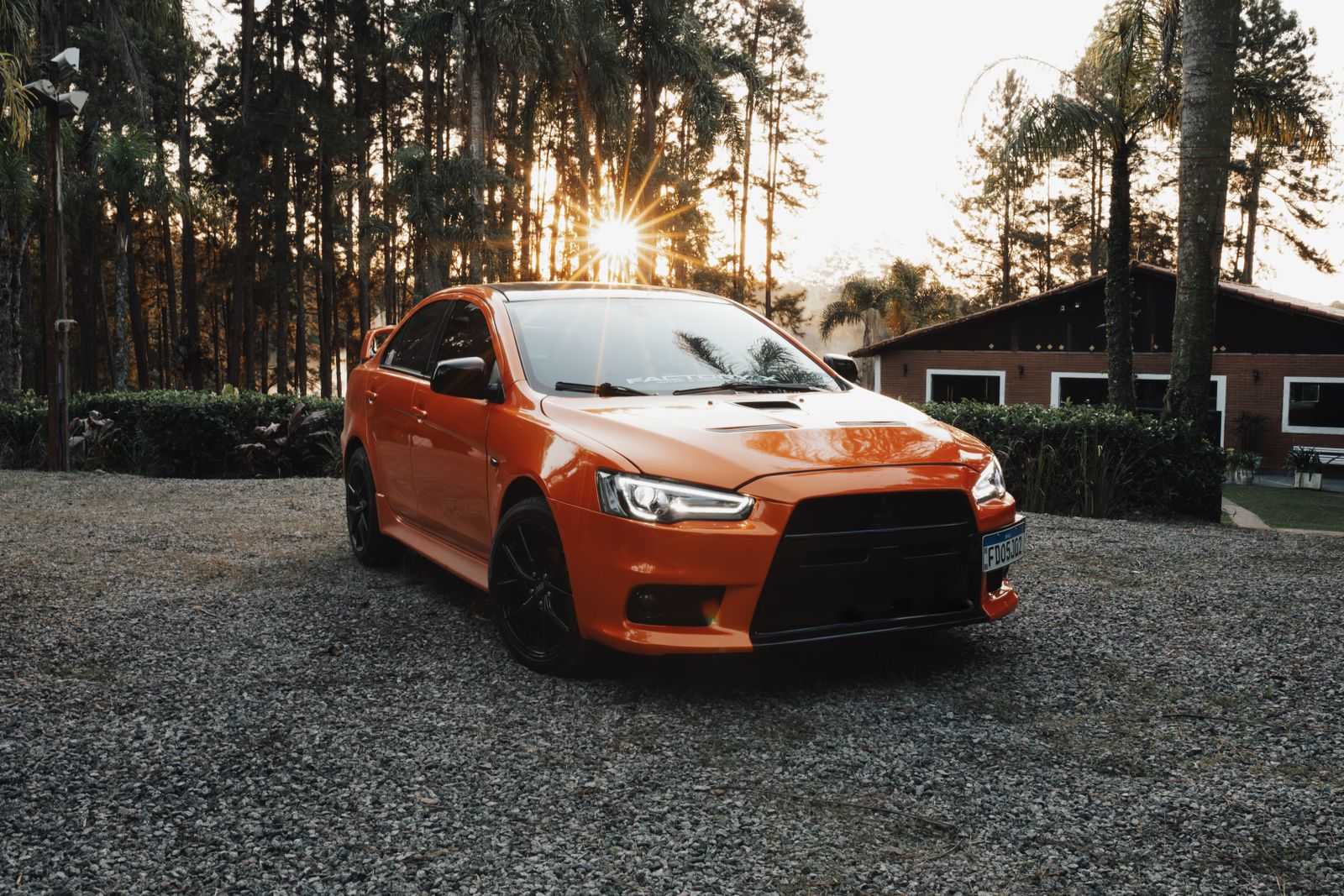 A striking orange sports sedan parked in a serene outdoor setting during sunset.