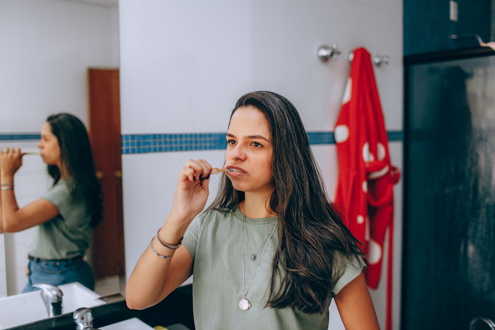 Young woman brushing teeth in a modern bathroom with a red towel hanging nearby.