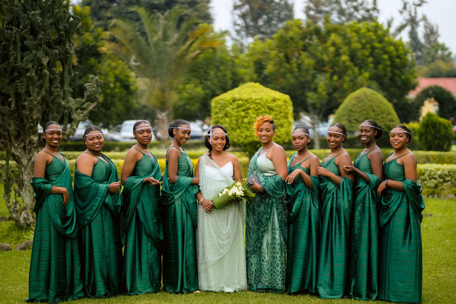 A group of bridesmaids and a bride in green dresses posing outdoors in a lush garden.