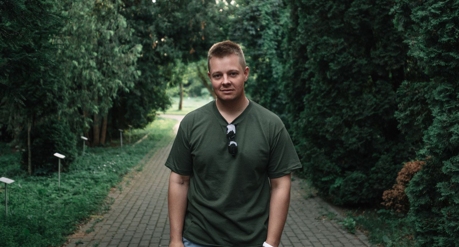 A young man in a green shirt strolling down a tree-lined path during the day.