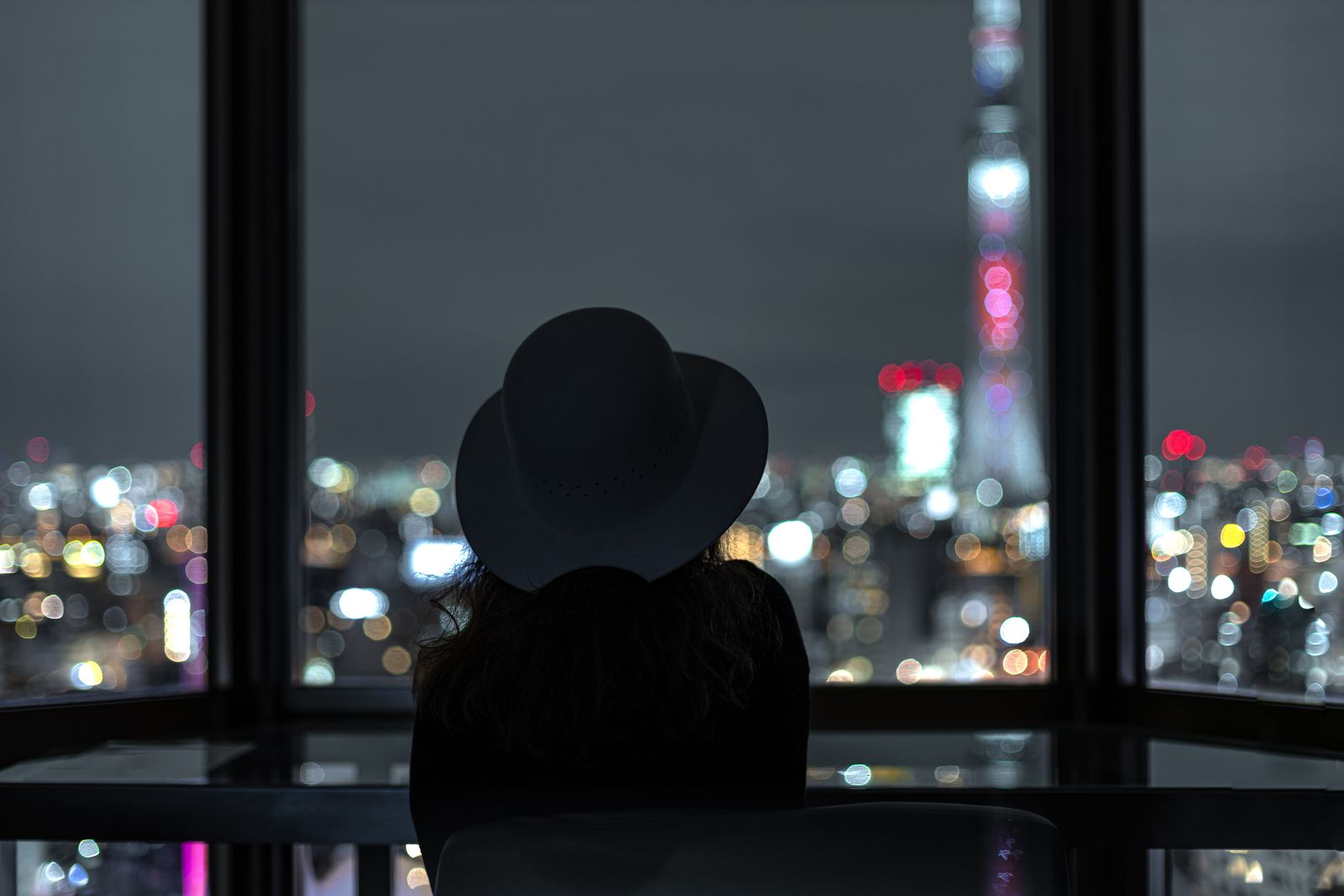 Silhouette of a woman looking at Tokyo city lights through a window at night.