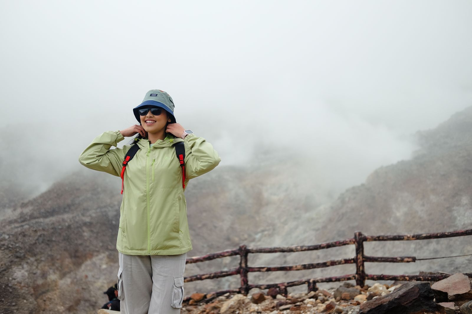 A woman in hiking gear enjoys a misty mountain view during a trek in West Java, Indonesia.