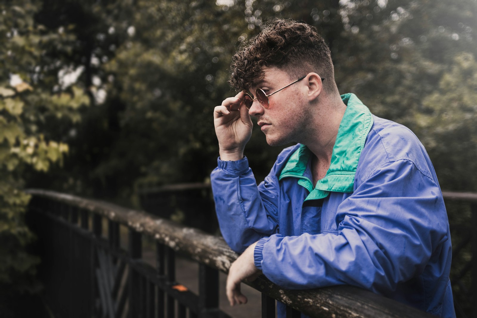 man in blue jacket sitting on brown wooden bridge during daytime