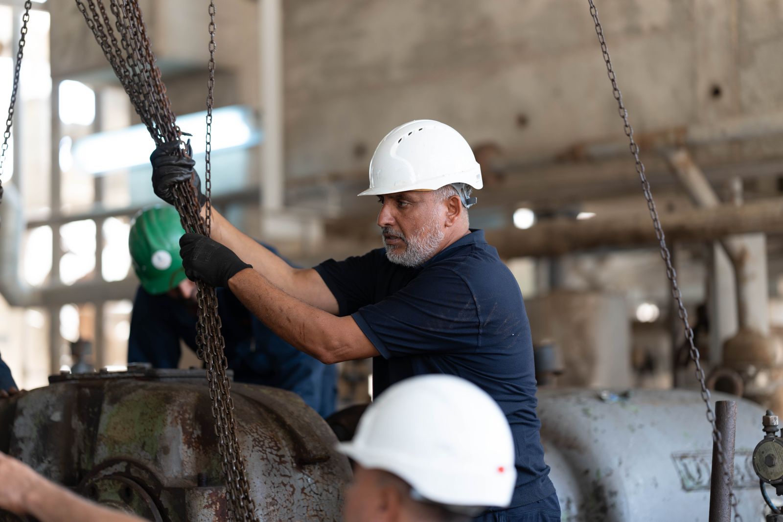 Workers with helmets operating chains in an industrial setting, Libya.