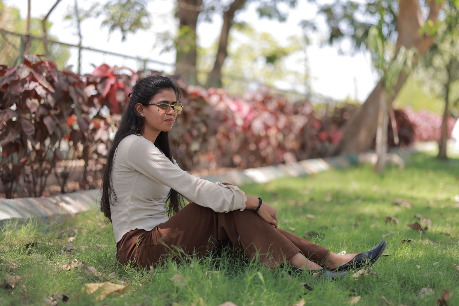 Young woman sitting on grass in the park, enjoying a sunny day outdoors with vibrant foliage.