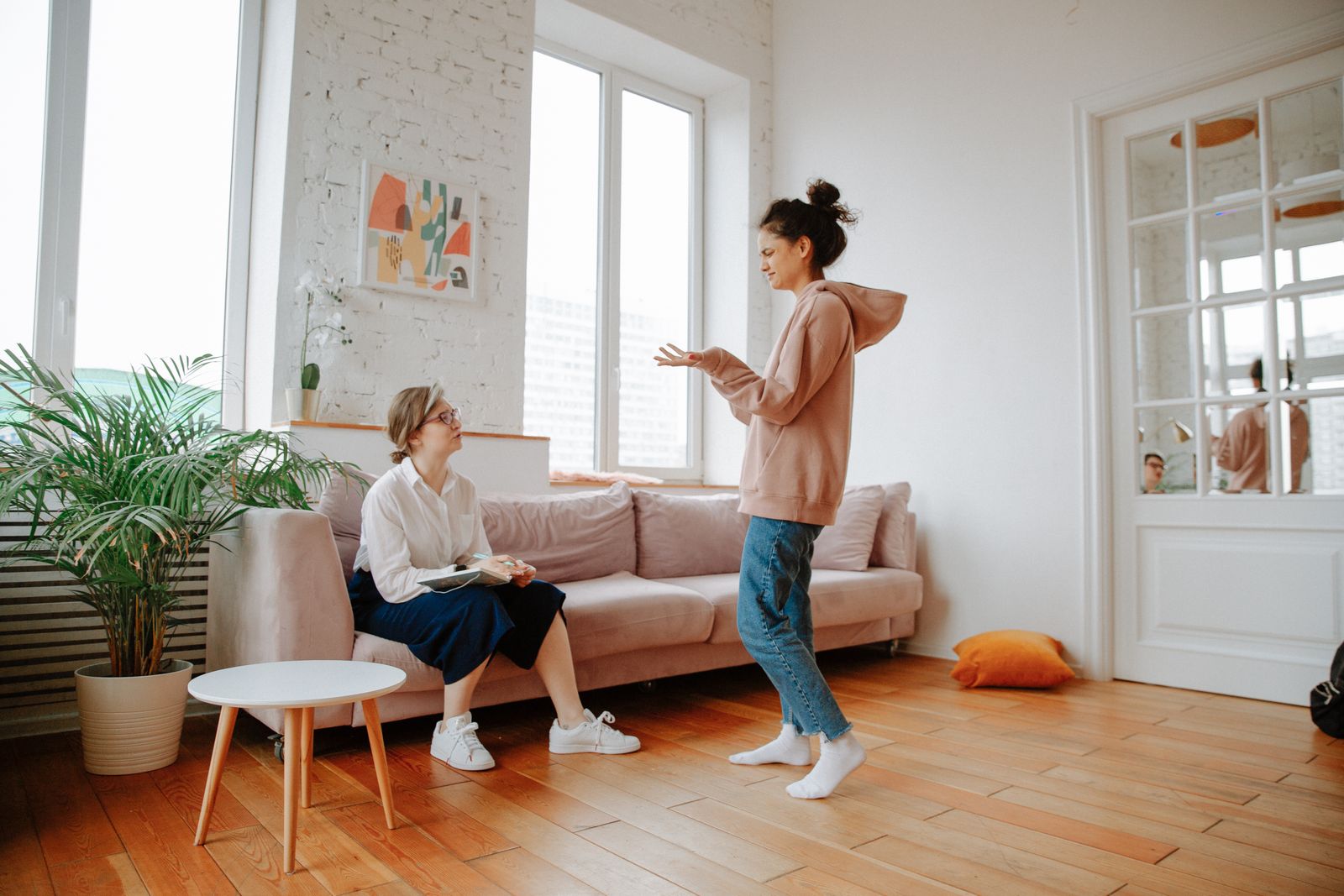 Two women in a relaxed therapy session in a bright, modern living room setting.