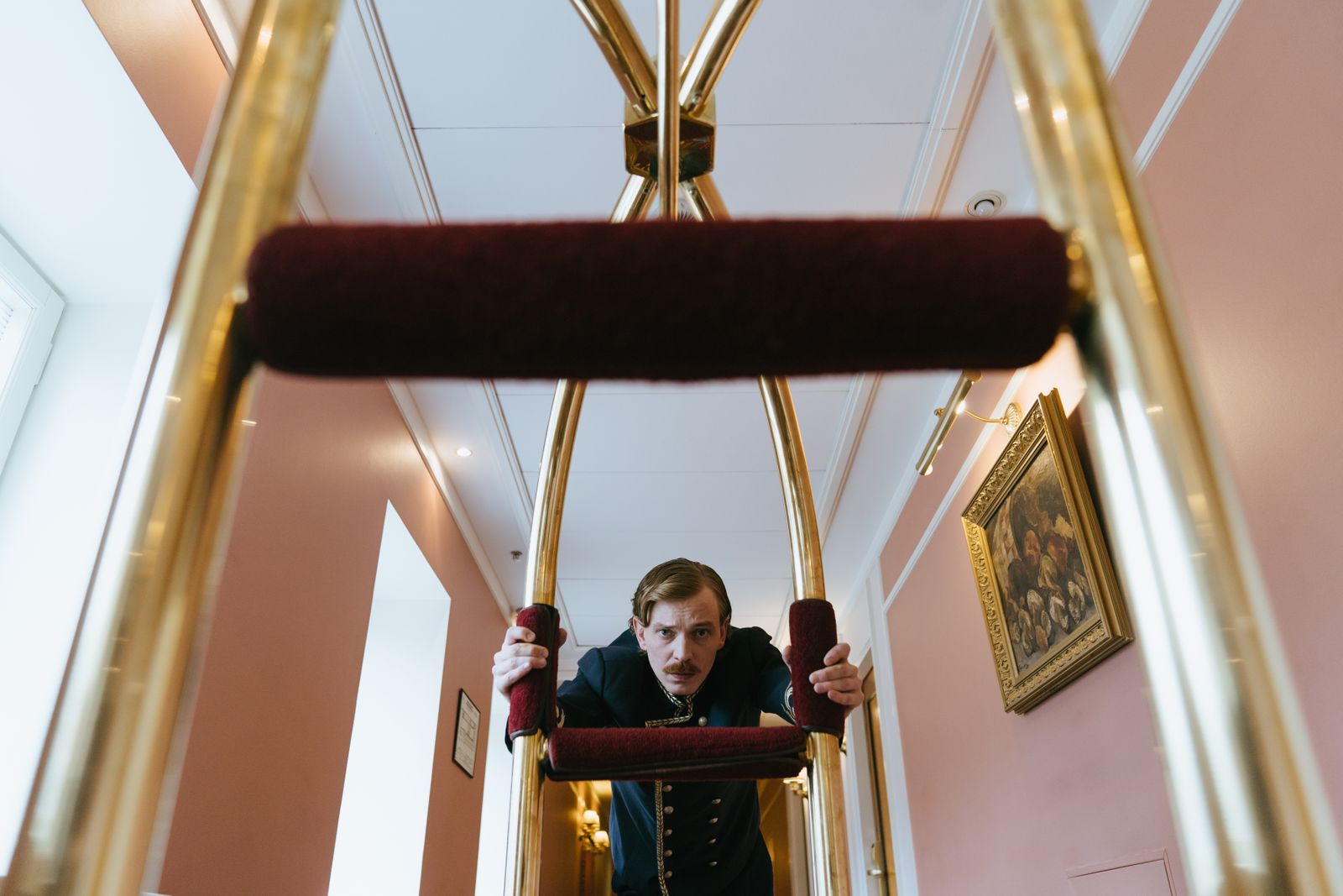 Hotel staff member in uniform pushing a luggage trolley through a corridor.