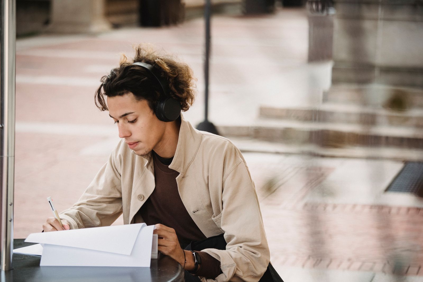 Serious young learner writing with pen on paper sheet of document for homework task in wireless headphones
