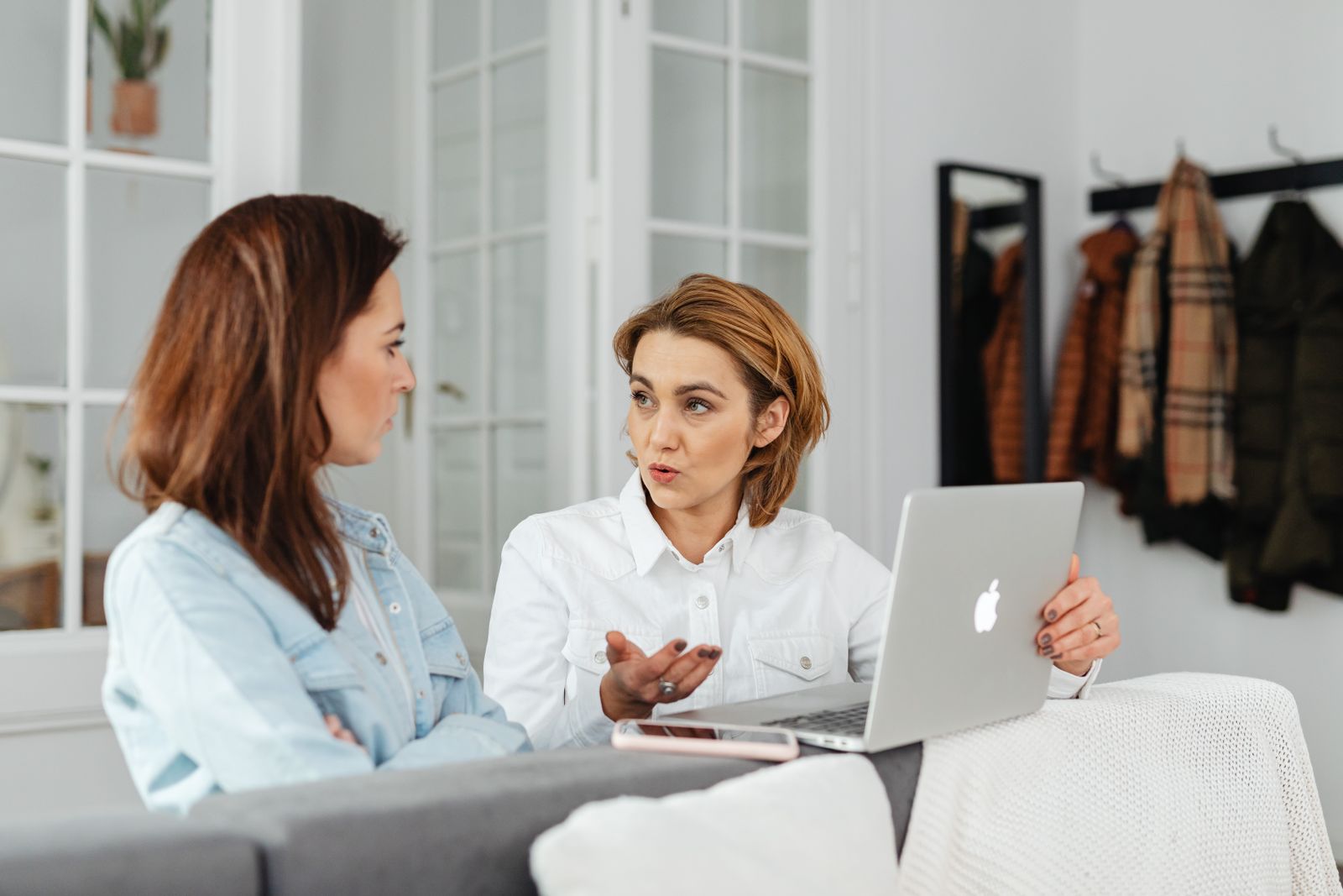 Two women having a conversation while working on a laptop in a cozy indoor setting.