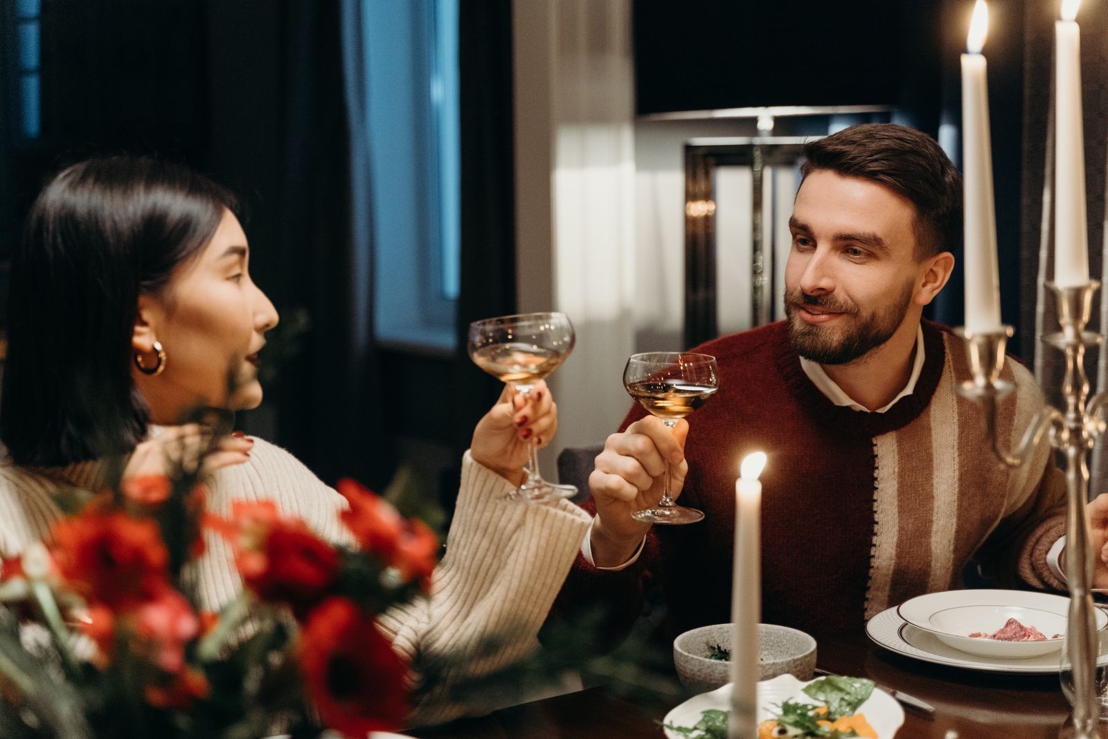 A couple enjoying a romantic dinner with candles, flowers, and wine glasses in an intimate setting.