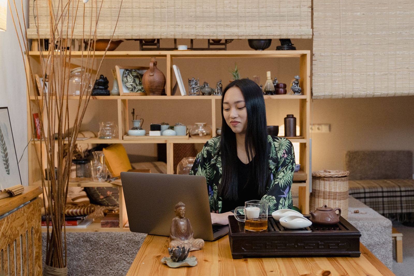 A young Asian woman working on her laptop in a cozy, decorated tea room setting.