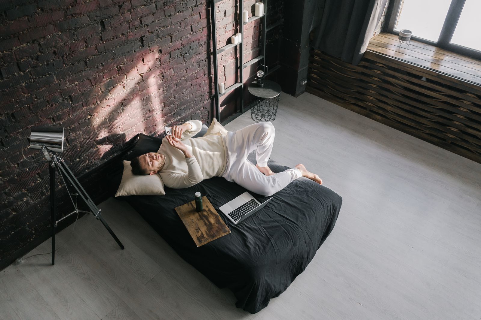 Adult man in casual attire texting on a smartphone while lying on bed in a modern loft.