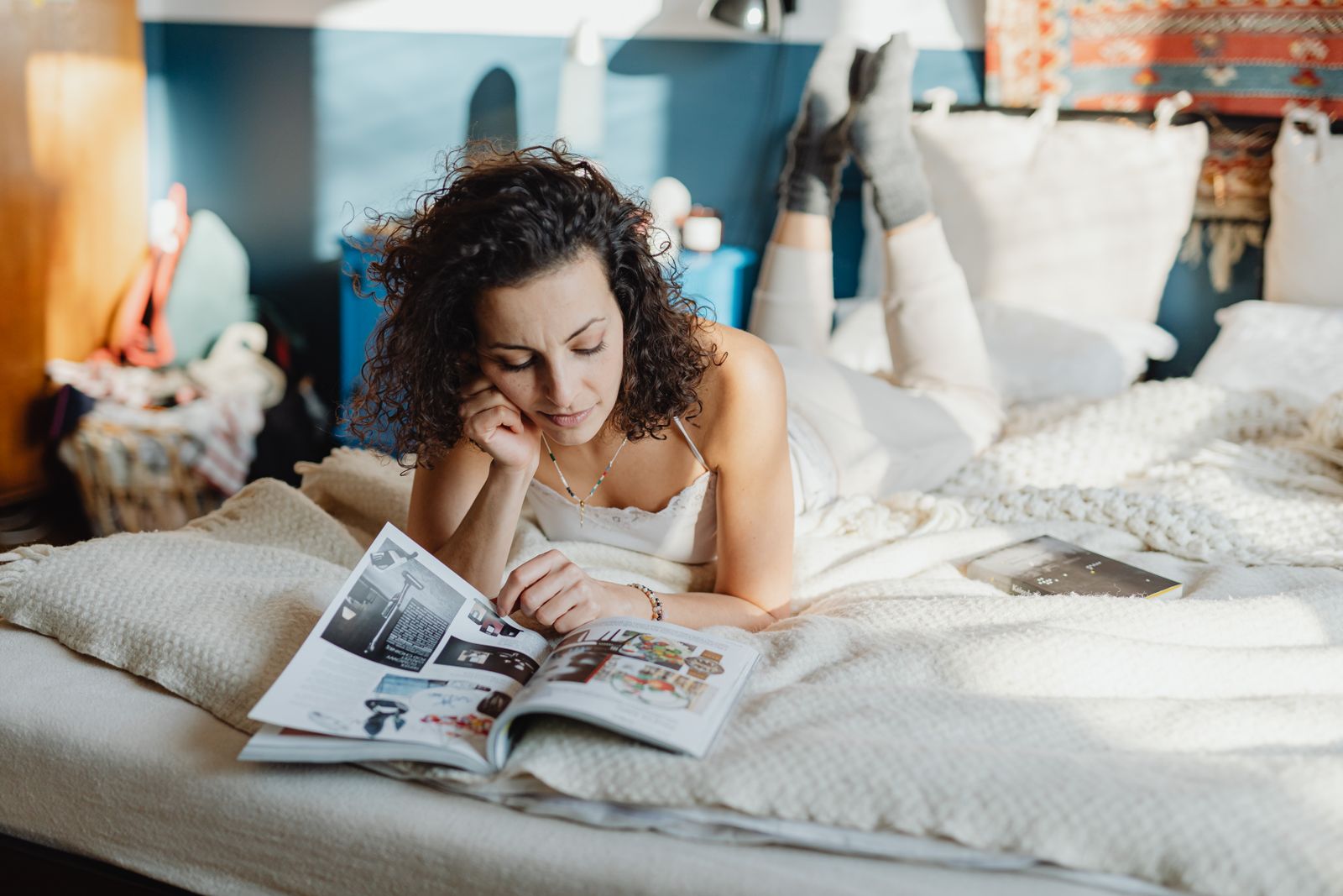 A woman relaxes on her bed, enjoying a magazine on a sunny day indoors.