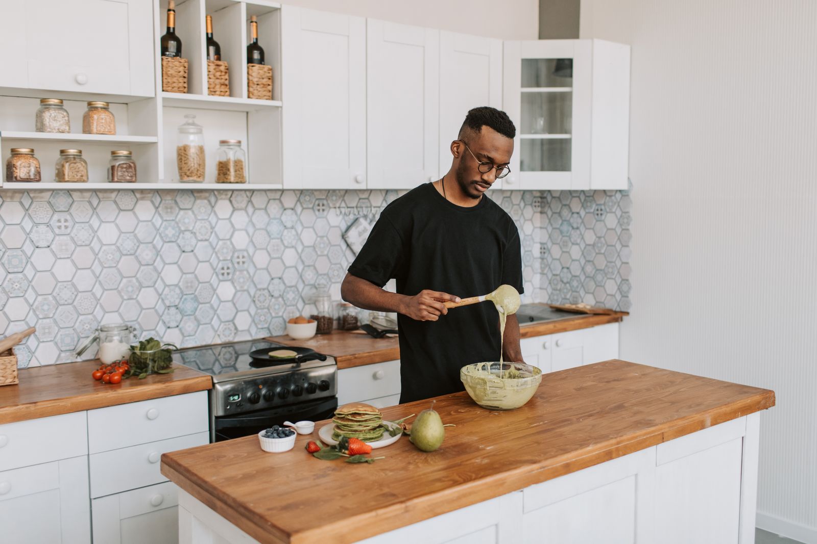 An adult man preparing food in a stylish kitchen, focusing on the mixing process.